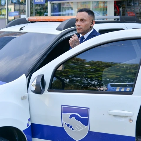 Segurança uniformizado no carro de patrulhamento da Prosev, olhando com atenção ao lado da porta e se comunicando com a equipe.